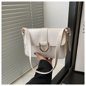 Détail du sac à rabat blanc texturé avec boucle métallique dorée en fer à cheval