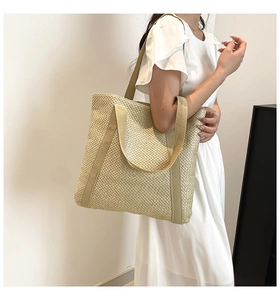 Détail d'un grand sac cabas tressé beige porté avec une robe d'été blanche et lumineuse