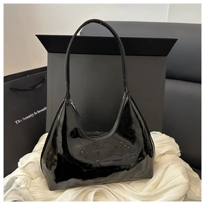 Detail of glossy black patent leather surface with subtle embossed logo on a hobo bag