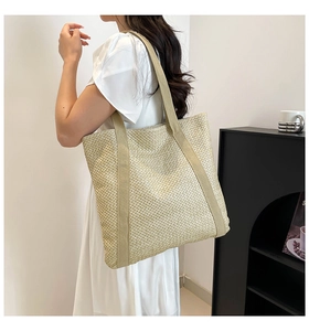 Détail du sac cabas en paille tissée avec de larges anses porté à l'épaule du mannequin