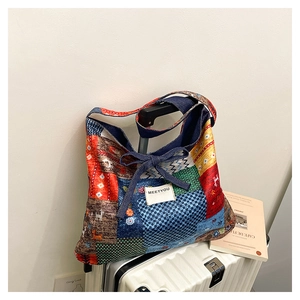 Detail of a patchwork tote bag with colorful patterns hanging on a white suitcase