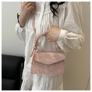 Detail of pink pleated crossbody bag with gold hardware worn with white lace dress