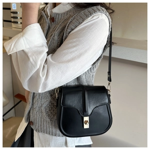 Detail of a black matte saddle bag with gold metal twist lock worn by a model