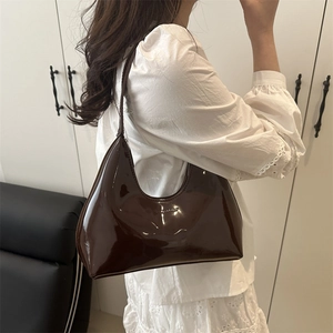 Glossy dark brown patent leather shoulder bag with sleek curved design worn by model
