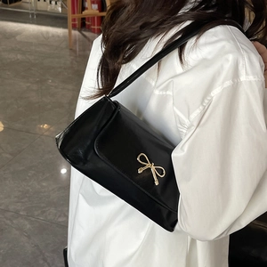 Sac baguette noir avec boucle nœud dorée porté par un mannequin en chemise blanche