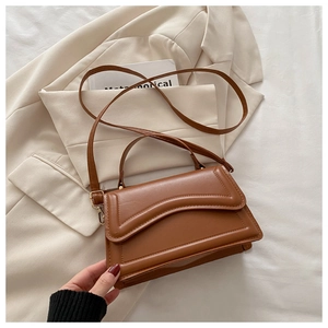 Détail du petit sac carré marron caramel à motif gaufré sur une veste de costume blanche