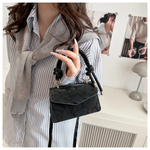 Detailed shot of textured black small square bag with round handle and gold hardware