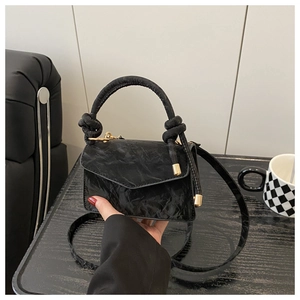 Detail of black pleated texture handbag with round knotted handle and gold hardware