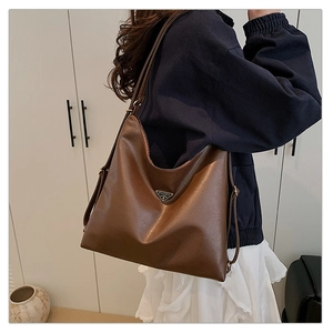 Detail of dark brown wax leather tote bag with a metal logo on model's shoulder