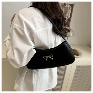 Detail of black shoulder bag with a gold bow buckle on smooth leather material