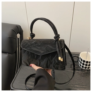Detail of black textured handbag with knot handle and elegant gold hardware accents
