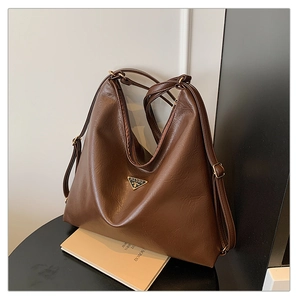 Macro detail of dark brown retro leather texture and triangular metal logo on tote bag