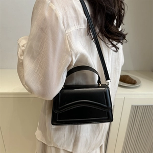 Sac carré bandoulière en cuir noir avec poignée supérieure porté par un mannequin