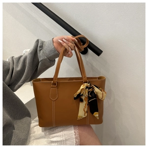 Detail of brown leather tote bag with white contrast stitching and decorative silk scarf