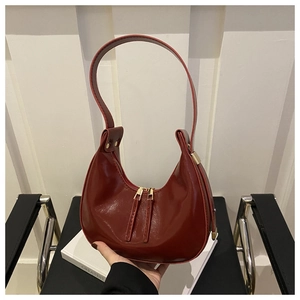 Detail of burgundy crescent shoulder bag in glossy patent leather with gold hardware