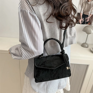 Retro black crossbody bag with pleated texture and circular woven handle on a minimalist model
