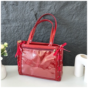 Detail of red patent leather tote bag featuring transparent PVC pocket and silk bows
