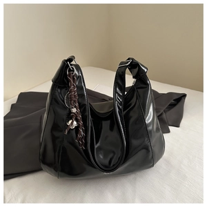 Dettaglio borsa hobo nera lucida con tracolla annodata e ciondolo su superficie bianca