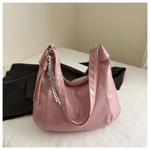 Dettaglio borsa hobo rosa chiaro in ecopelle con ciondolo a racchetta su letto bianco