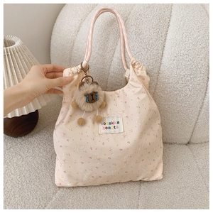 Detail of floral tote bag with cute plush rabbit charm and woven straps on a sofa