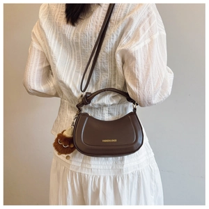 Brown leather crescent hobo bag with gold text and plush charm worn by a model