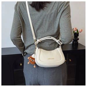 Detail of a beige leather crescent hobo bag with adjustable strap and plush charm on model