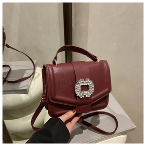 Macro view of burgundy pebble leather handbag featuring a square rhinestone buckle