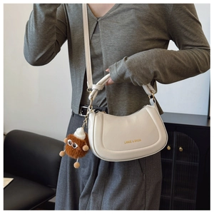 Detail of white leather half-moon bag with gold logo and funny brown plush doll charm
