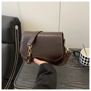 Detail view of dark brown leather handbag with wavy flap edge and gold hardware