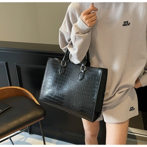 Detail of black crocodile pattern tote bag featuring glossy texture and handle strap
