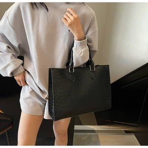 Detail of black crocodile embossed tote bag featuring elegant gold metal hardware