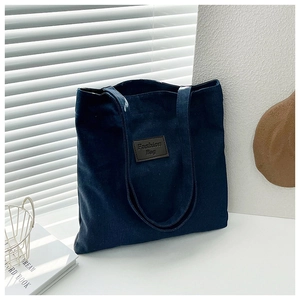 Detailed view of navy blue denim tote bag with brown leather label on front