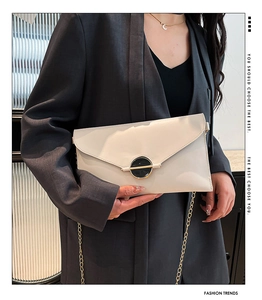 Pochette enveloppe crème chic avec chaîne dorée portée sur un blazer gris foncé