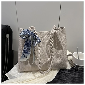 Detail shot of beige woven tote bag with silk scarf on a soft white silk fabric