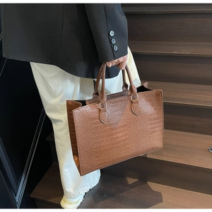 Brown crocodile embossed tote bag detail held by model on wooden stairs for daily commute