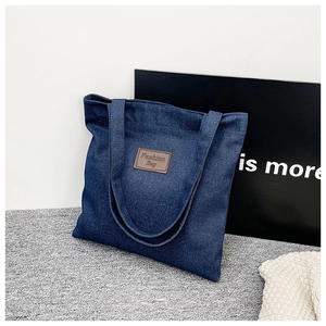 Detail of dark blue denim tote bag featuring a brown leather label with fashion lettering