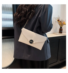 Sac enveloppe blanc porté par un mannequin sur fond urbain avec boucle dorée chic