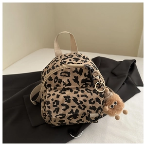 Detail of leopard print corduroy mini bag with a plush monster charm on textured bedding