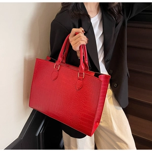Detail view of large red tote bag with crocodile texture and golden hardware accents