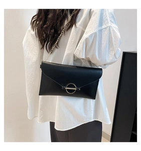 Détail d'un sac enveloppe noir en cuir avec chaîne dorée et fermoir en métal rond