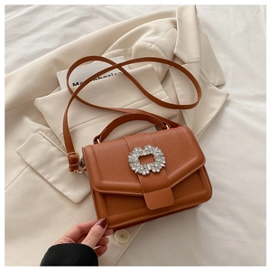Detail of brown textured crossbody bag with sparkling rhinestone buckle on a beige blazer