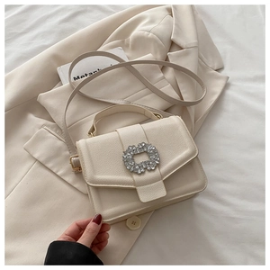 Detail of a beige lychee leather handbag with a large rhinestone buckle on a blazer