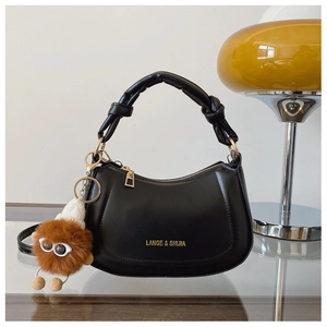 Detail of black crescent handbag featuring knotted handle, gold logo, and plush charm