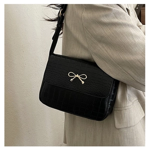 Détail du sac à bandoulière noir en cuir croco avec fermoir nœud doré sur un mannequin