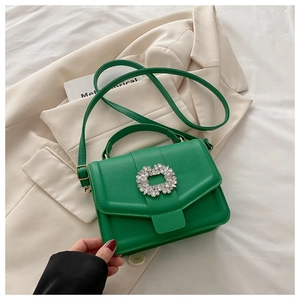 Close-up of green lychee leather handbag with floral rhinestone buckle on beige blazer