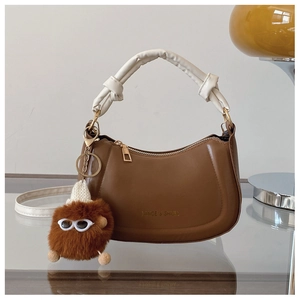 Close-up of brown half-moon bag with white knotted handle and plush monster charm