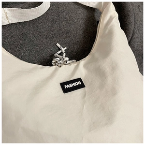 Close-up of minimalist cream nylon crescent bag with black FASHION logo and strap detail