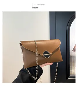 Gros plan d'un sac enveloppe marron avec chaîne dorée et boucle métallique centrale