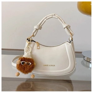 Detail of white half-moon leather bag featuring a knotted handle and plush monster charm