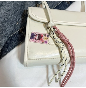Detail of cream PU shoulder bag featuring creative colorful woven rope pendants and a cute tag